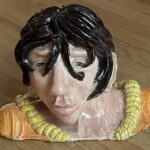 Chad, a plaster head of guy with brown hair hanging in his eyes and seashell neckless 9’ H X 12” W